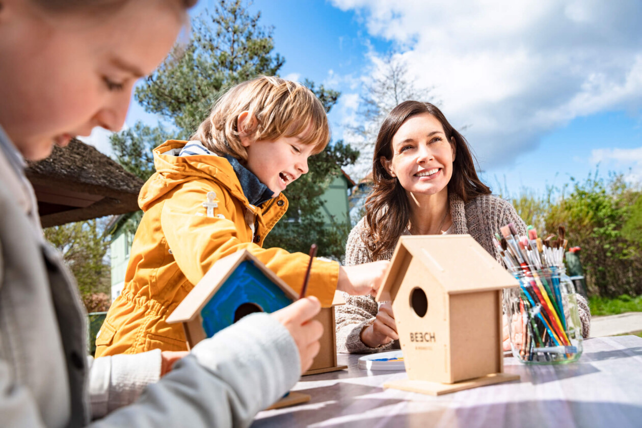 Zwei Kinder und eine Frau beim Basteln eines Vogelhaus